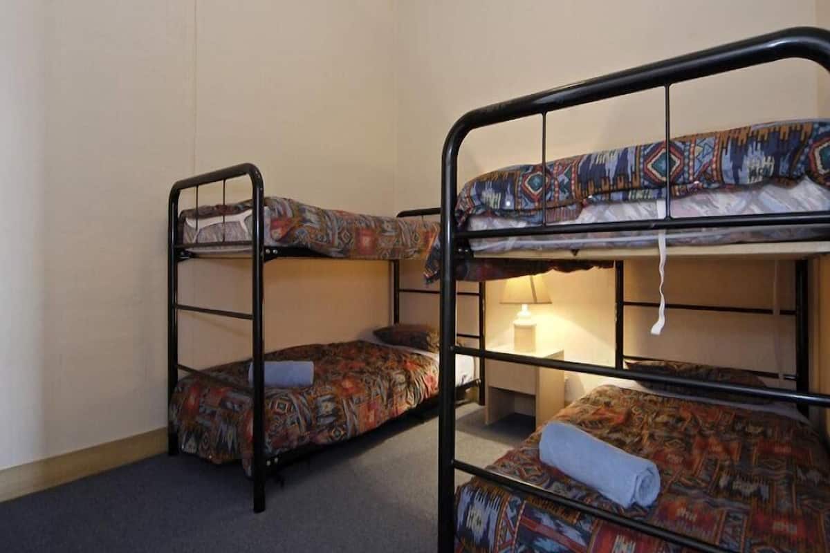 A room with three bunk beds, each with patterned bedding. There is a lamp on the floor between the beds.