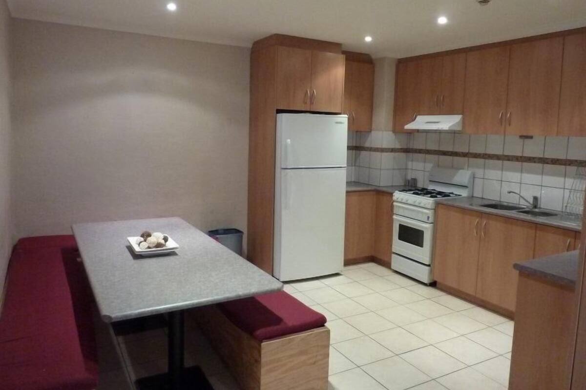 A compact kitchen with wooden cabinets, a white refrigerator, a stove, and a dining table with a bench.