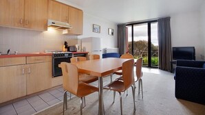 A compact kitchen with wooden cabinets, a dining table with four chairs, a built-in stove, and a refrigerator. There is a balcony with a view of greenery. - Arlberg Hotham (Hotham Heights)