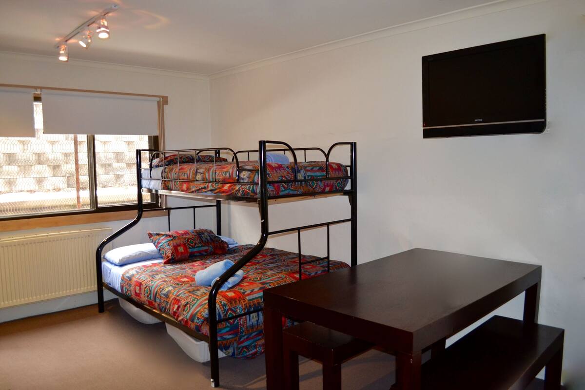 A bunk bed with colorful bedding, a wooden table, and a TV mounted on the wall.