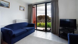 A living room with a blue sofa, a television on a stand, and a sliding glass door leading to a balcony. - Arlberg Hotham (Hotham Heights)