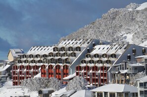 Un hôtel moderne doté d’une façade géométrique originale, de nombreux balcons et offrant une vue imprenable sur une montagne enneigée.