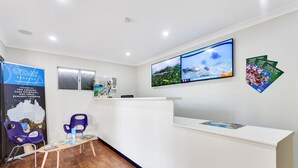 A reception area with a white counter, two purple chairs, a wooden table with brochures, and a large screen displaying travel content.