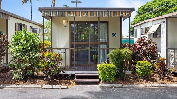 A modern building with a glass entrance, numbered 96, surrounded by well-maintained landscaping and palm trees.