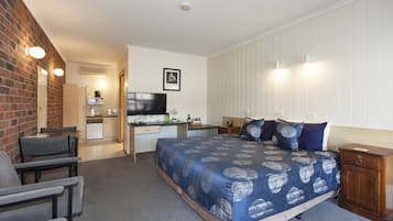 A bedroom with a large bed, a desk, a chair, and a small kitchenette.