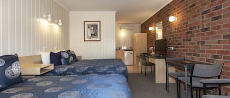 Habitación de hotel con dos camas, un escritorio, una silla, una kitchenette pequeña y una pared de ladrillo.