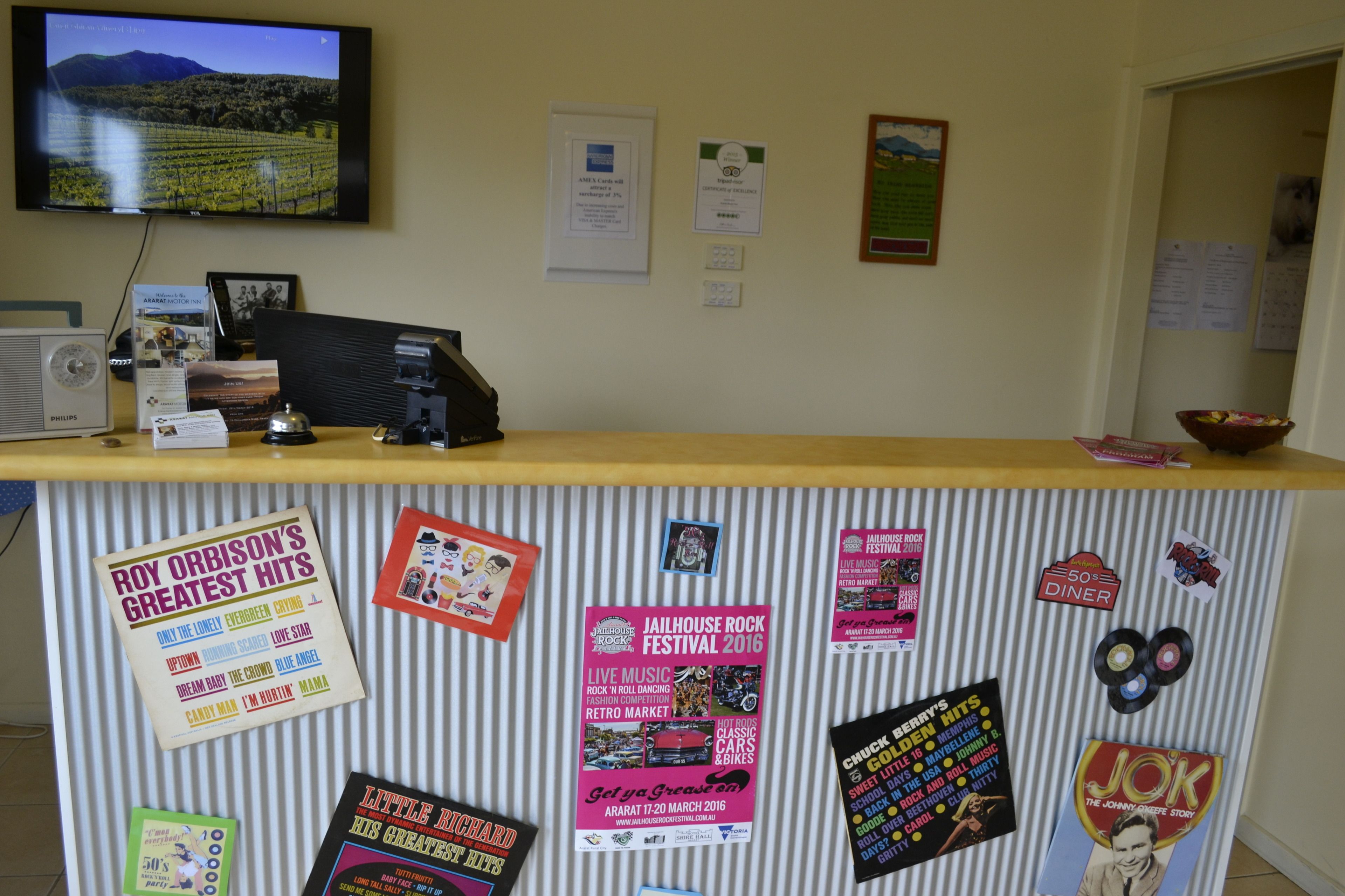 A reception desk with various posters and a television displaying a vineyard landscape.