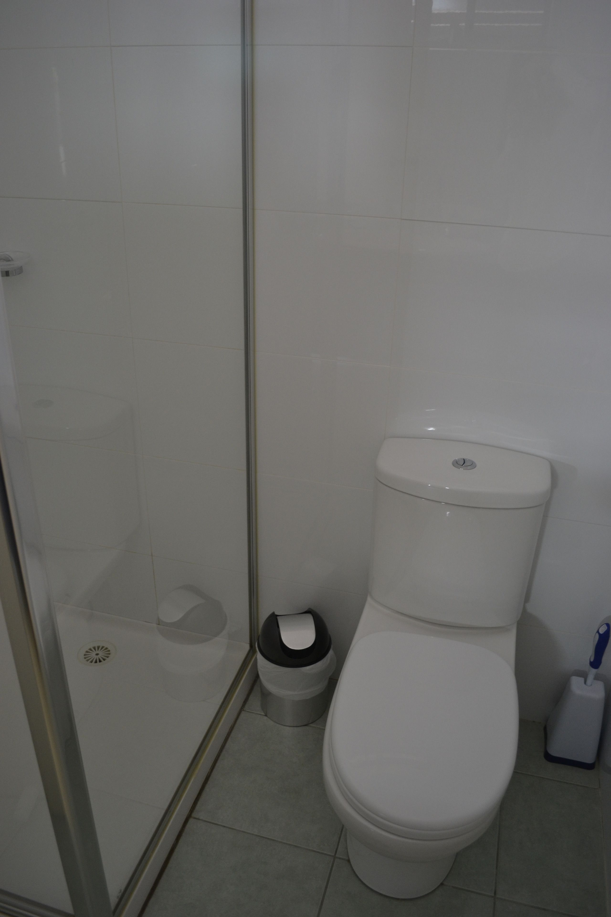 A bathroom with a toilet, a trash bin, and a shower area.