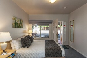 Habitación de hotel con cama, lámparas de noche, un cuadro, una puerta que da al exterior y un espejo en la pared.