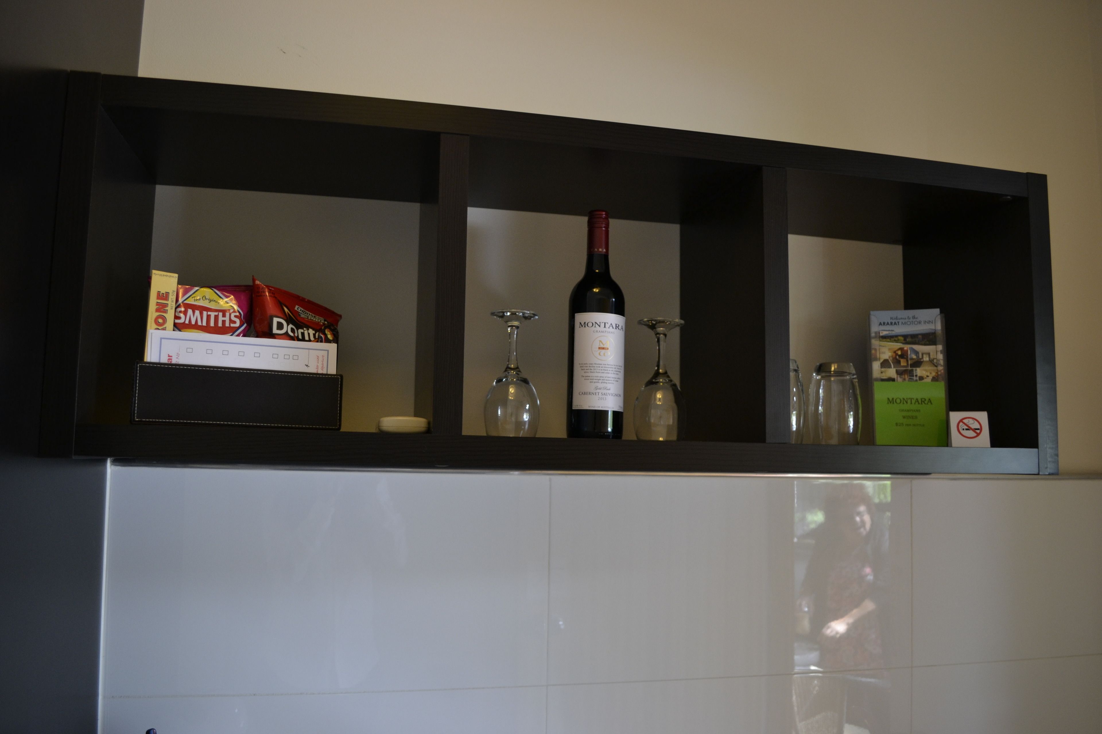 A kitchen shelf with a wine bottle, glasses, and packaged snacks.