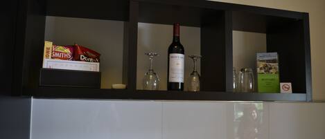 A kitchen shelf with a wine bottle, glasses, and packaged snacks.