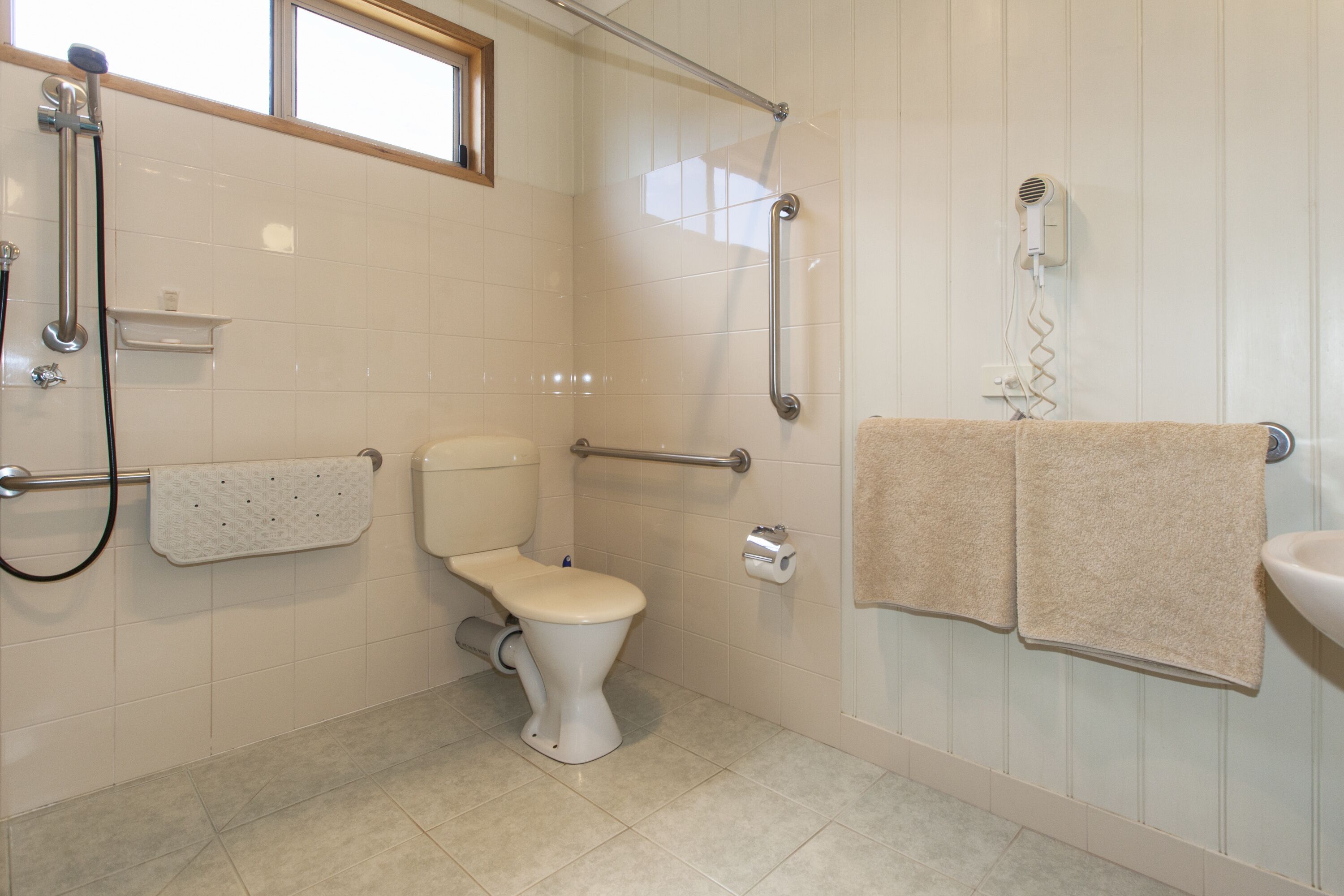 A bathroom with a toilet, grab bars, a shower, a towel rack, and a sink.