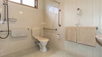 A bathroom with a toilet, grab bars, a shower, a towel rack, and a sink.