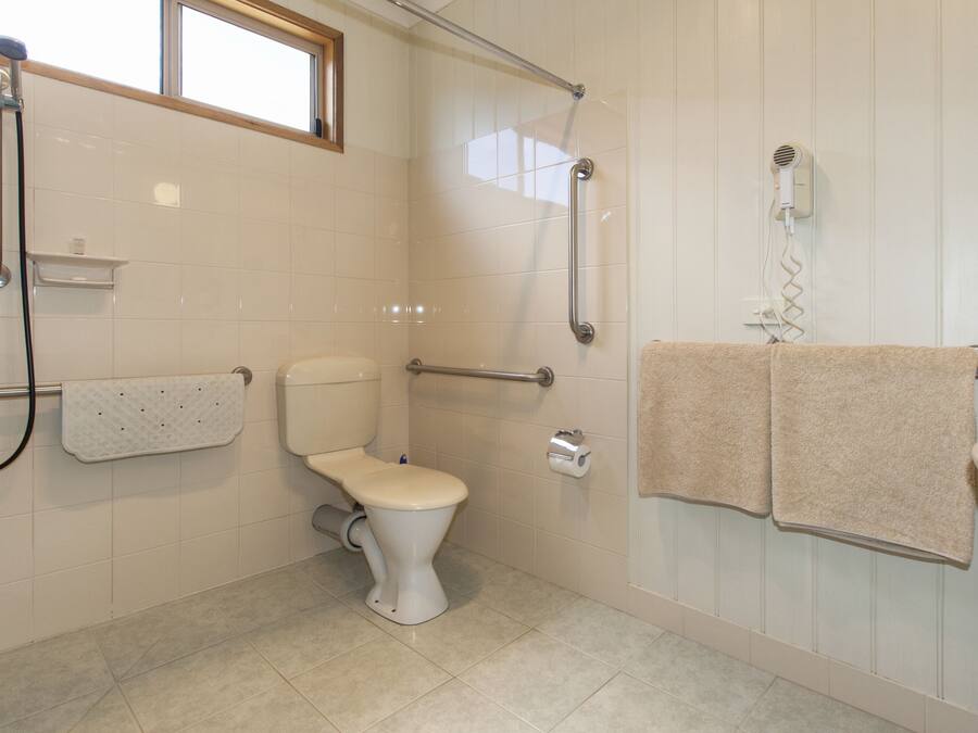 A bathroom with a toilet, grab bars, a shower, a towel rack, and a sink.
