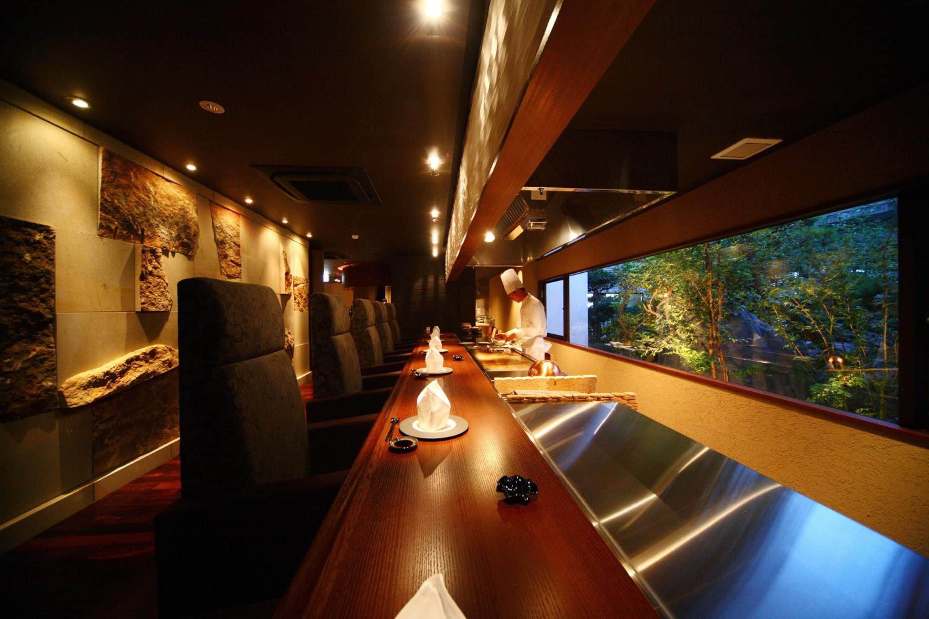 Un ristorante con un lungo tavolo di legno, sedie e vista su alberi attraverso una finestra.