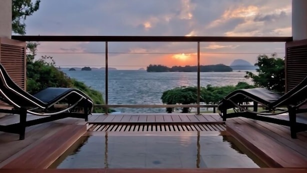 A pool area with two lounge chairs and a view of the sunset over the sea.
