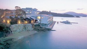 A coastal hotel with a stone wall, a large building with multiple windows, and boats in the water.