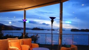 A balcony with wicker furniture, a round table, and a view of a body of water with distant land.