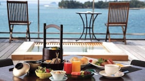 A dining table with a meal, two chairs, a small table, and a view of the sea.