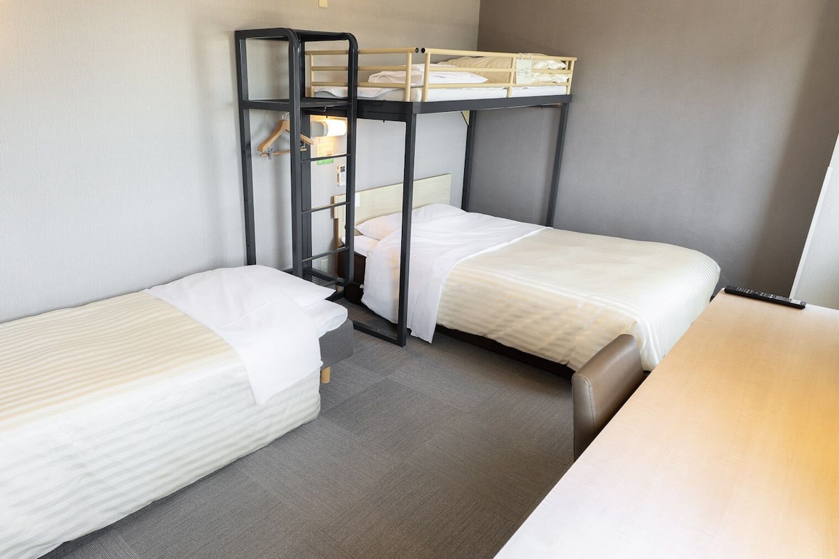 A room with two single beds, a bunk bed, a desk, and a wall-mounted light fixture.