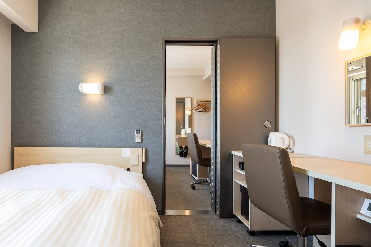 A hotel room with a bed, desk, chair, and a mirror.