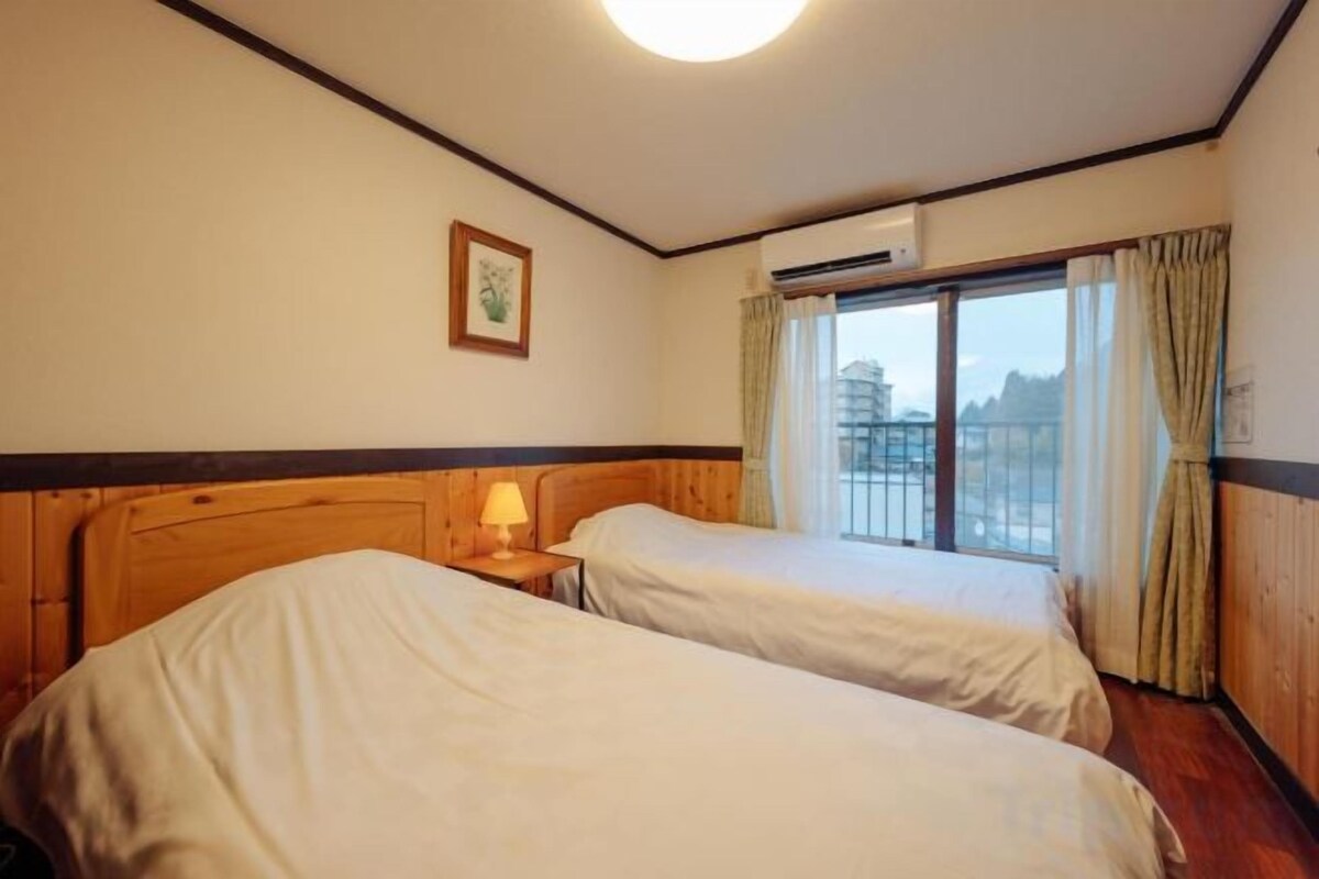 Habitación de hotel con dos camas, una ventana con cortinas, un cuadro en la pared y un equipo de aire acondicionado.