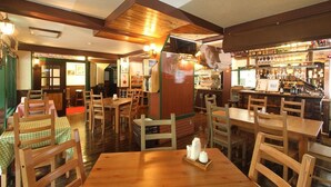 Un restaurante con mesas y sillas de madera, una zona de bar con botellas y una barra.