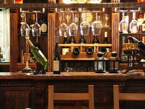 Un bar con estanterías llenas de botellas y vasos, una botella verde y una barra de madera.