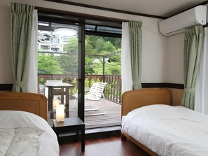 Habitación de hotel con dos camas, un balcón con mesa y sillas, y vistas a zonas verdes y edificios.