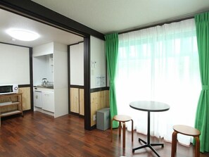A room with a dining table, two stools, a microwave, a washing machine, and a kitchen area. - Hotel Morgenrot (Kobe)