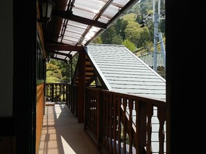 A wooden balcony with a sloped roof, a railing, and a view of trees and power lines. - Hotel Morgenrot (Kobe)