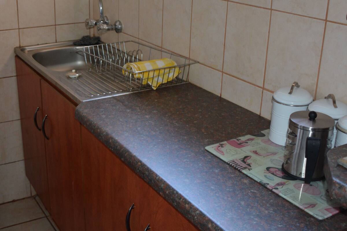 A kitchen with a granite countertop, a stainless steel sink, a drying rack, and two white ceramic containers.