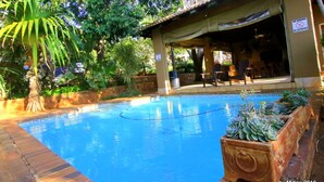 A pool area with a covered seating area, surrounded by lush greenery and a stone wall.