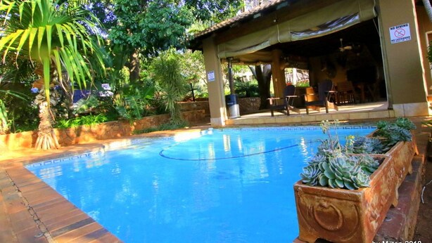 A pool area with a covered seating area, surrounded by lush greenery and a stone wall.