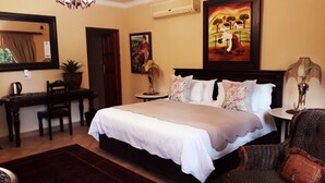 A hotel room with a large bed, a desk, a chair, a lamp, and a painting on the wall.