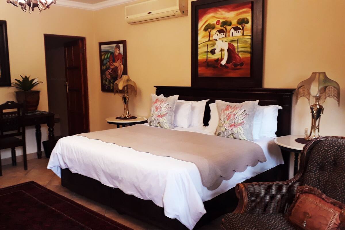 A hotel room with a large bed, a desk, a chair, a lamp, and a painting on the wall.