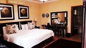 A hotel room with a large bed, a desk, a chair, a mirror, and two framed pictures on the wall.