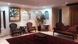 A living room with a red carpet, two armchairs, a sofa, a coffee table, and a potted plant.