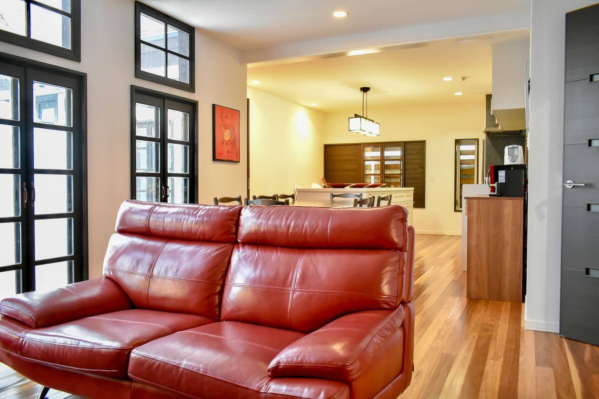 Un amplio salón con un sofá de cuero rojo, ventanas grandes, una zona de cocina y una mesa de comedor.