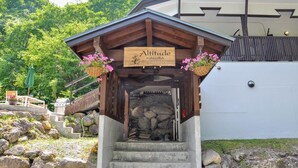 Un pabellón de madera con un letrero que dice "Altitude Hakuba" y una chimenea de piedra.