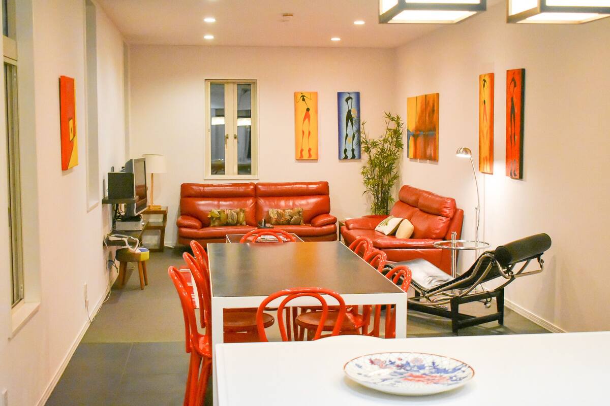 Un comedor con una mesa larga y sillas rojas, un sofá y un televisor.