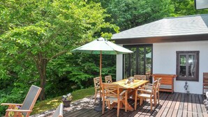 Una terraza de madera con una mesa y sillas, rodeada de exuberante vegetación.