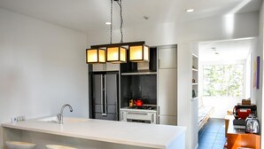 Una cocina moderna con una isla central, electrodomésticos de acero inoxidable y una lámpara colgante.