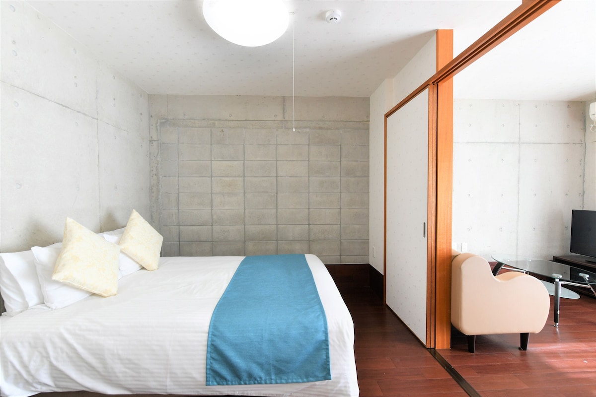 A modern hotel room with a bed, a chair, a television, and a sliding door.