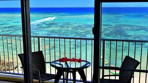 A balcony with a view of the ocean, two chairs, and a table with red flowers. - Churaumi On The Beach Motobu (Motobu)