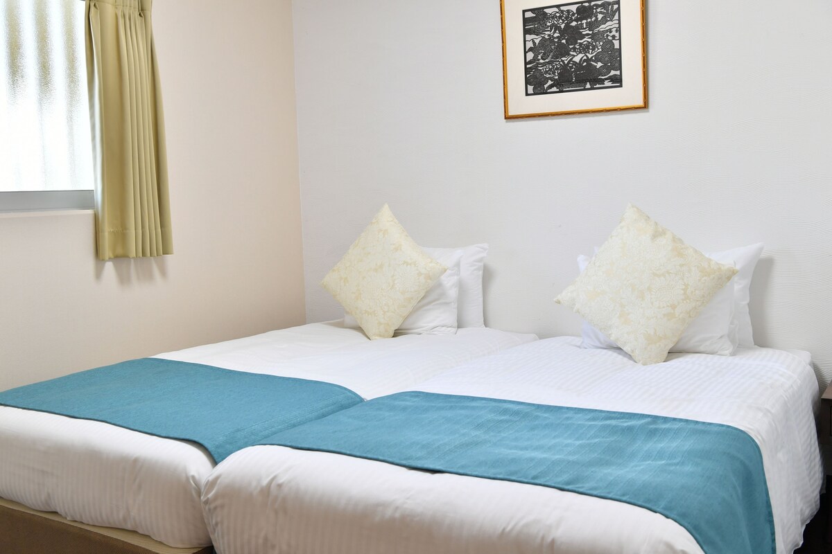 A double bed with white and teal bedding, two pillows, and a framed picture on the wall.