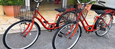 Two red bicycles with black seats and baskets, parked on a paved surface.