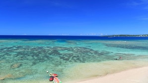 Una playa con aguas turquesas cristalinas, una orilla arenosa y una isla a lo lejos.