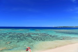 Una playa con aguas turquesas cristalinas, una orilla arenosa y una isla a lo lejos.