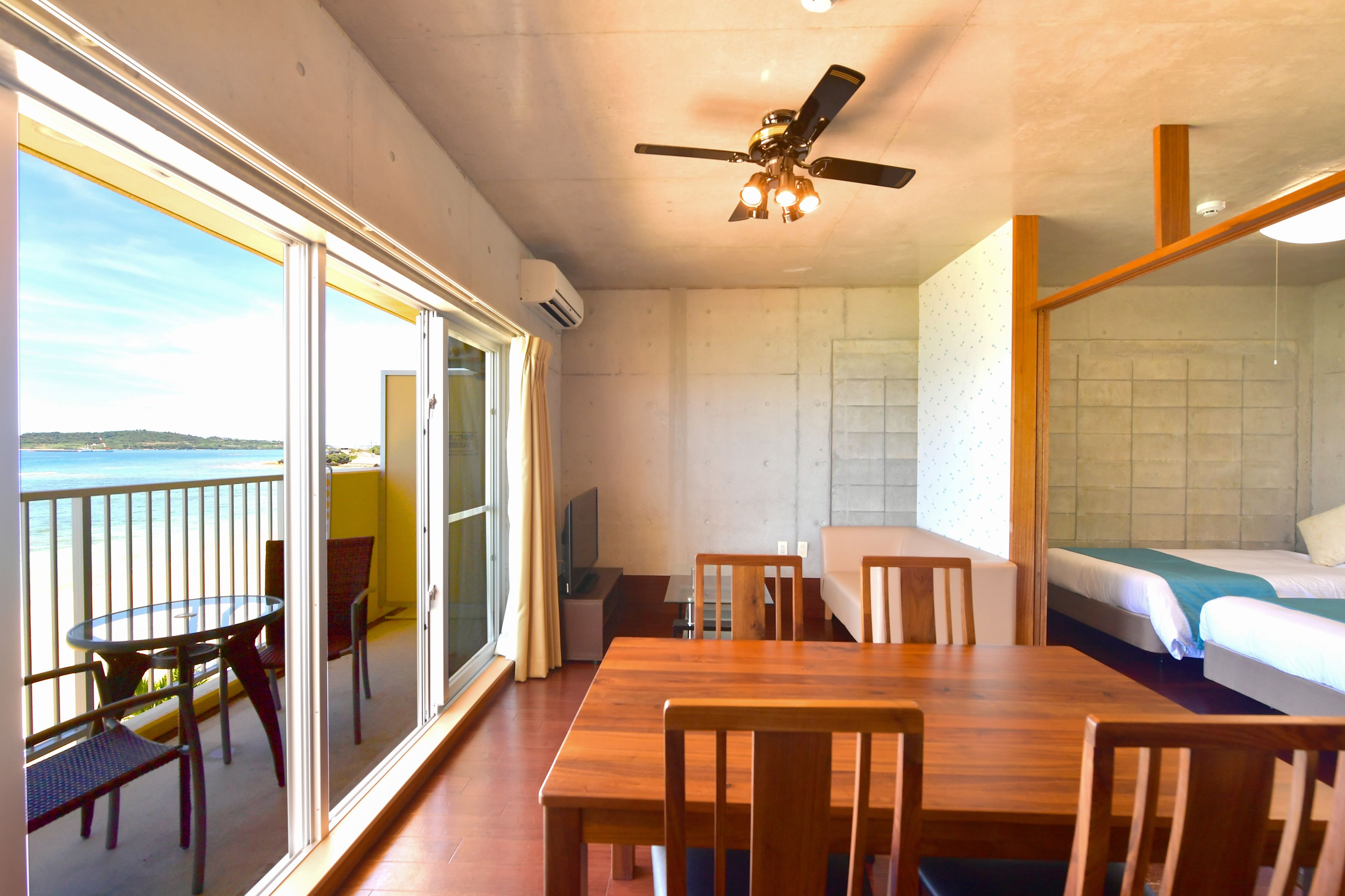 A room with a balcony, a dining table, and a bed.
